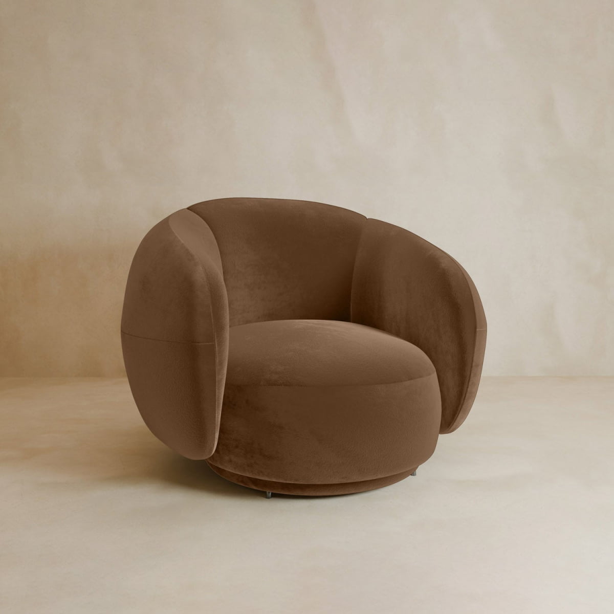 The Clara Armchair features plush brown velvet upholstery with rounded, cushioned arms and a supportive backrest, set against a neutral beige background for a stylish contemporary look.