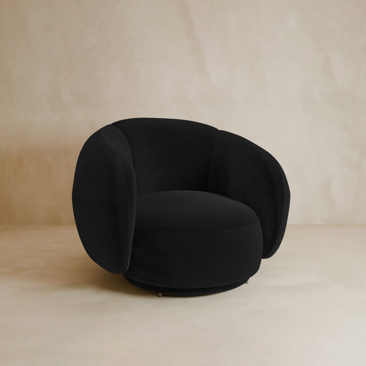 A modern Clara Armchair with plush, oversized cushions and luxurious black velvet upholstery sits on a light beige background.