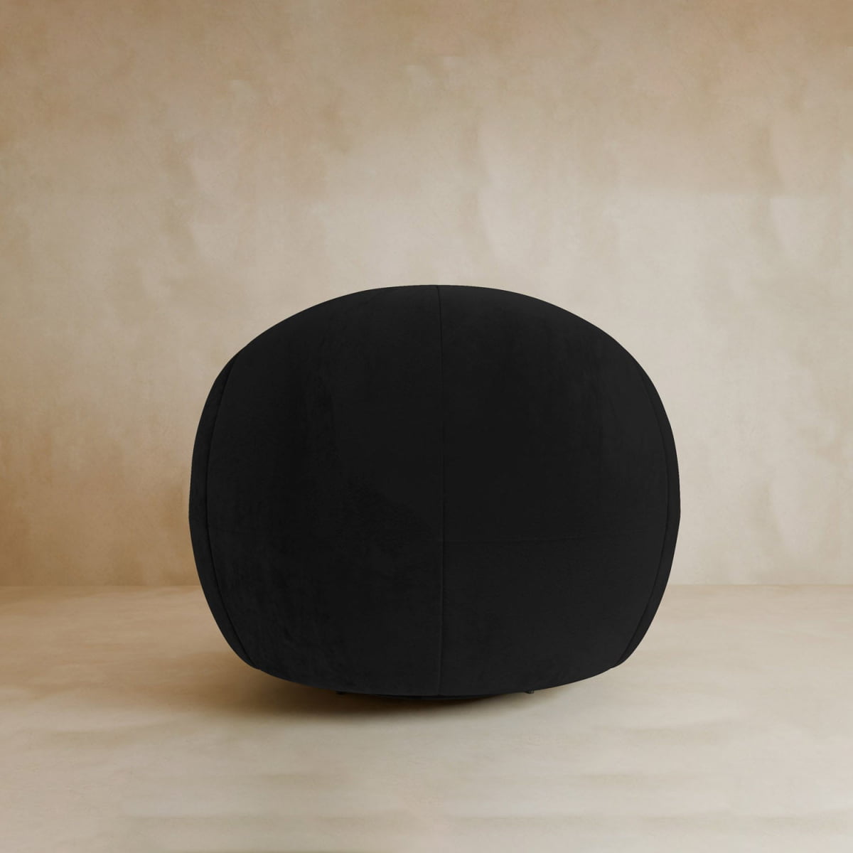 The Clara Armchair, with its smooth velvet upholstery in black and rounded design, sits on a light-toned floor by a beige textured wall, bringing contemporary style to the space.
