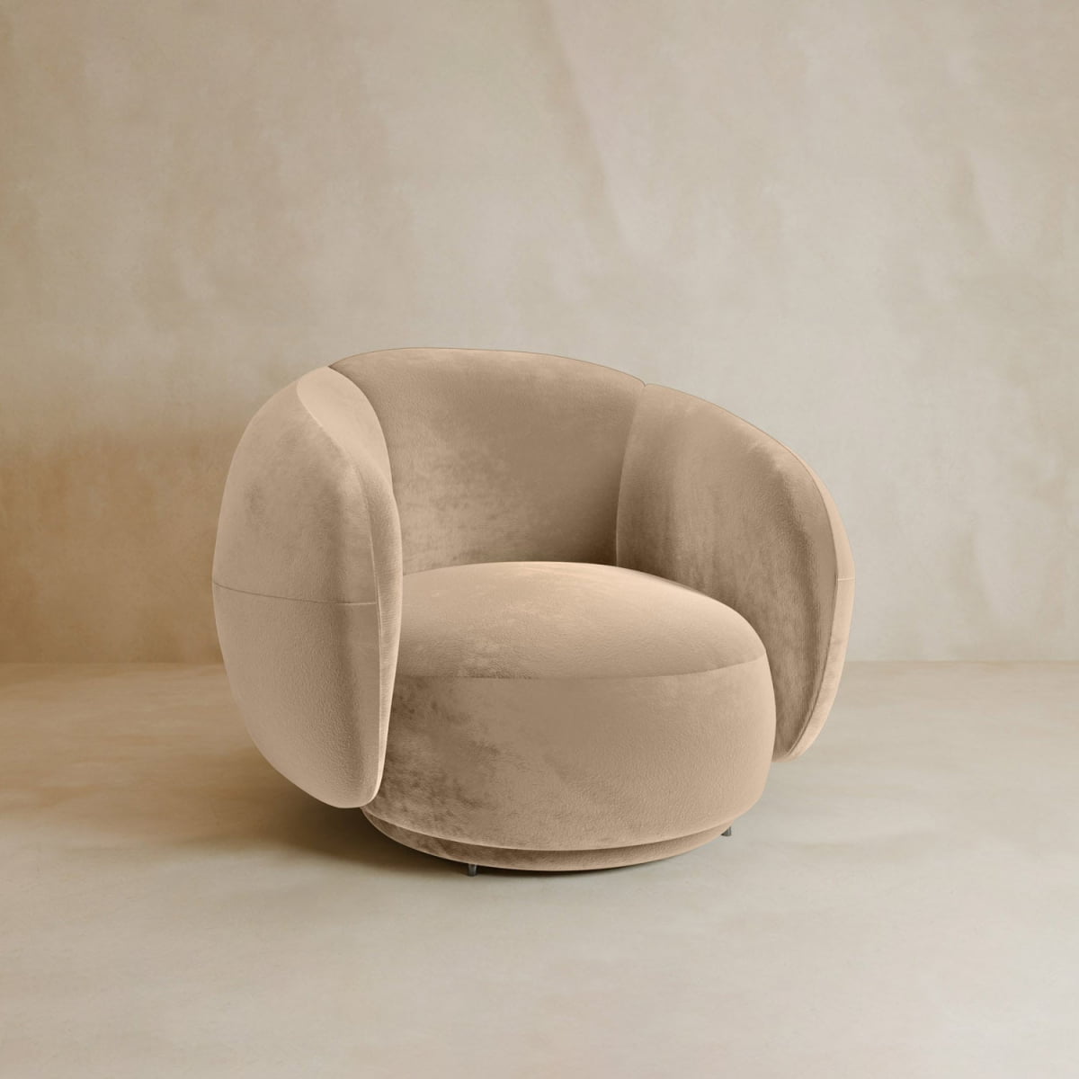 The Clara Armchair features beige velvet upholstery, plush rounded armrests, and a curved backrest. Set against a neutral background, it’s perfect for enhancing any contemporary living space.