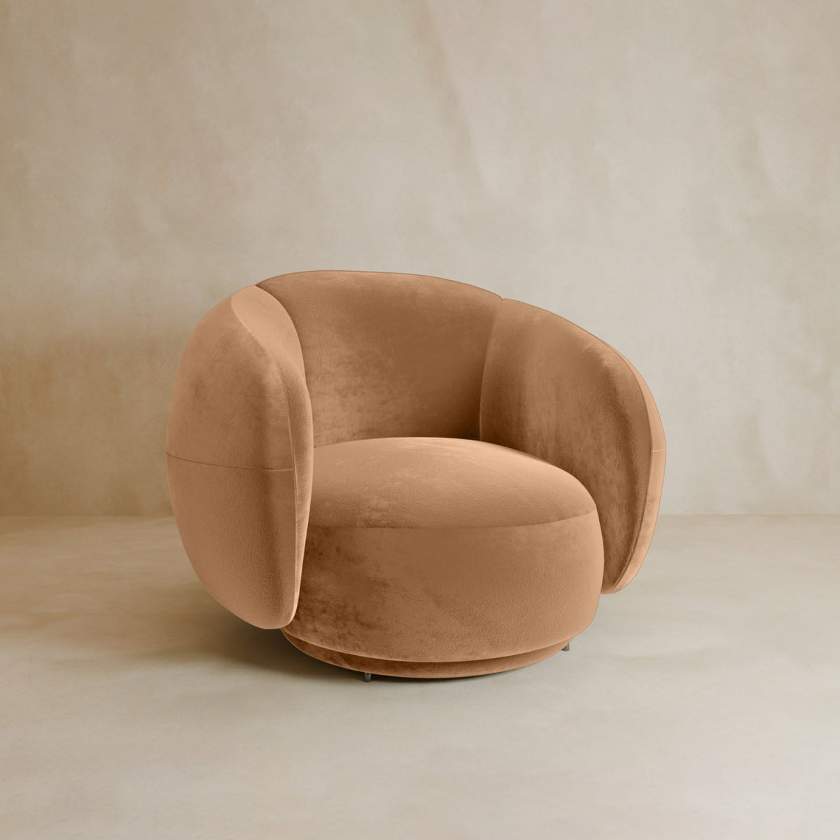 The Clara Armchair features a modern round design with plush, curved sides and camel velvet upholstery, shown against a neutral beige background for contemporary style.