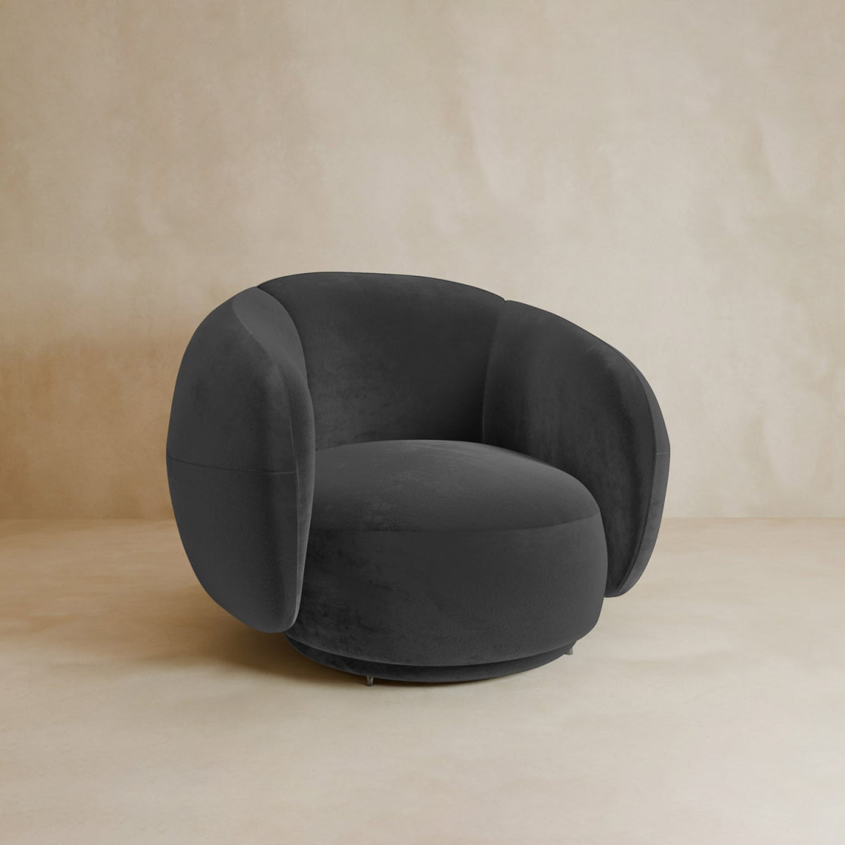 The Clara Armchair is a modern, dark gray velvet chair with wide rounded arms, a circular seat, contemporary style, and swivel feature, shown against a light beige textured background.