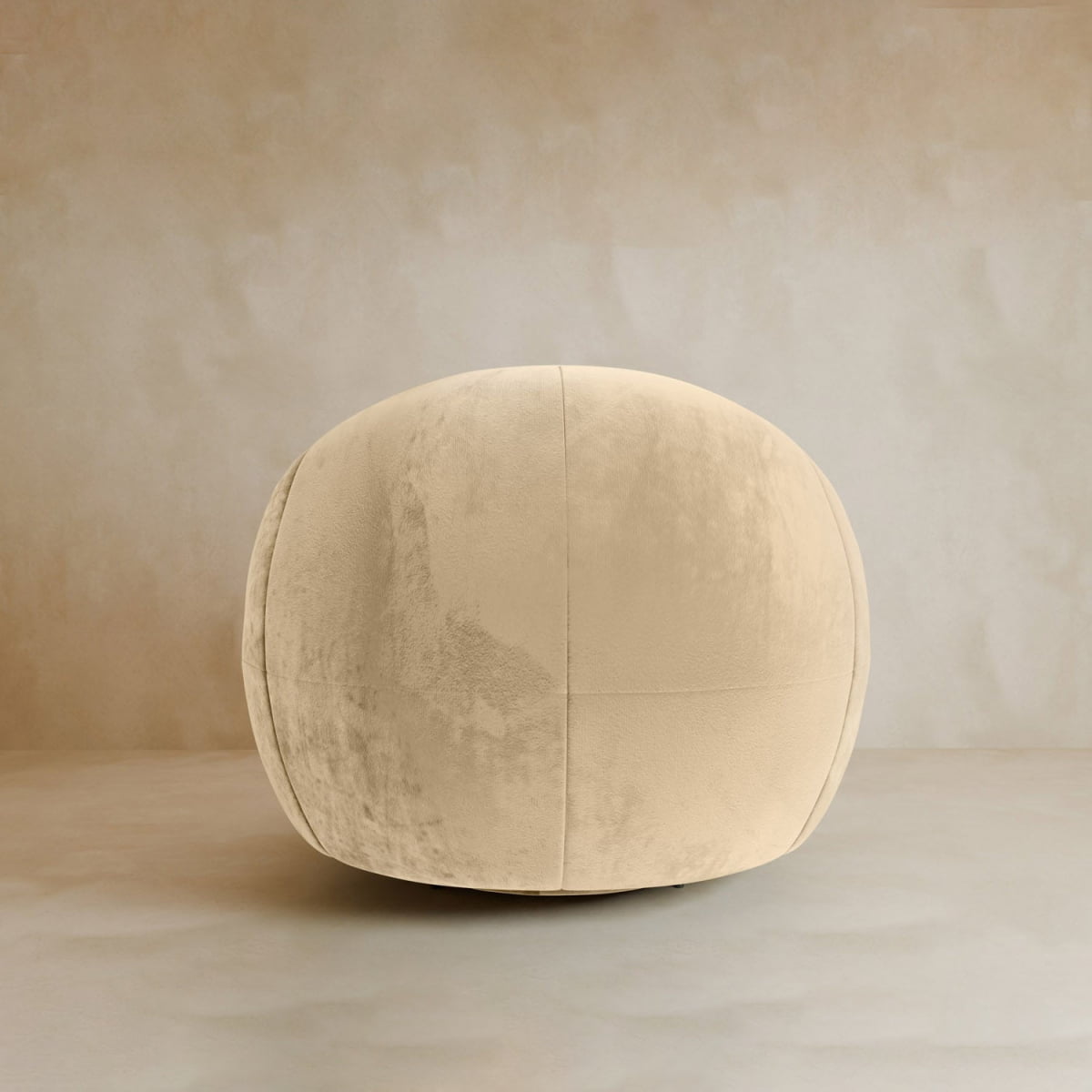 The Clara Armchair features plush velvet upholstery in beige, a round silhouette, and a soft, velvety texture. Placed on a matching floor with a neutral textured wall background, it adds contemporary style to any space.