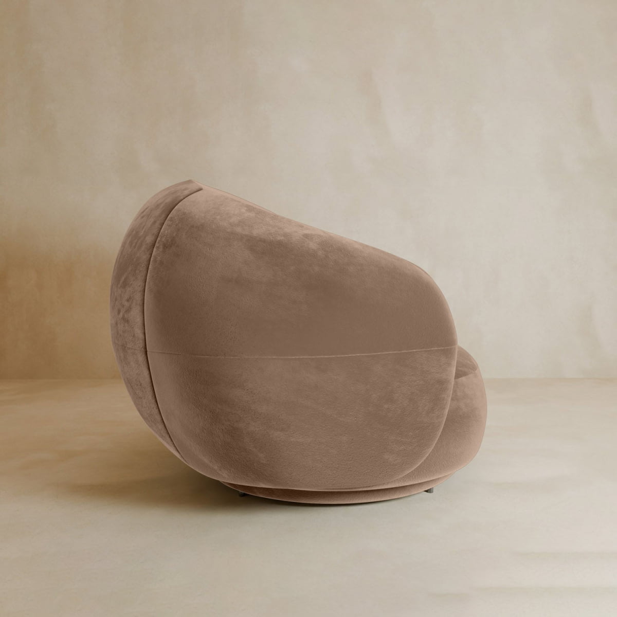 The Clara Armchair features a modern, rounded design with plush beige velvet upholstery, set on a matching floor against a neutral background—ideal for enhancing any contemporary space.