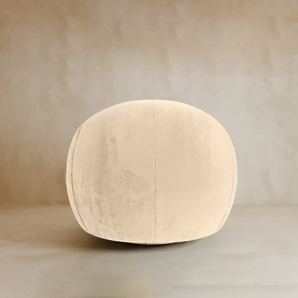 A large, round ottoman with plush velvet upholstery sits on a neutral floor, adding contemporary flair to the beige background—perfectly complementing the Clara Armchair.