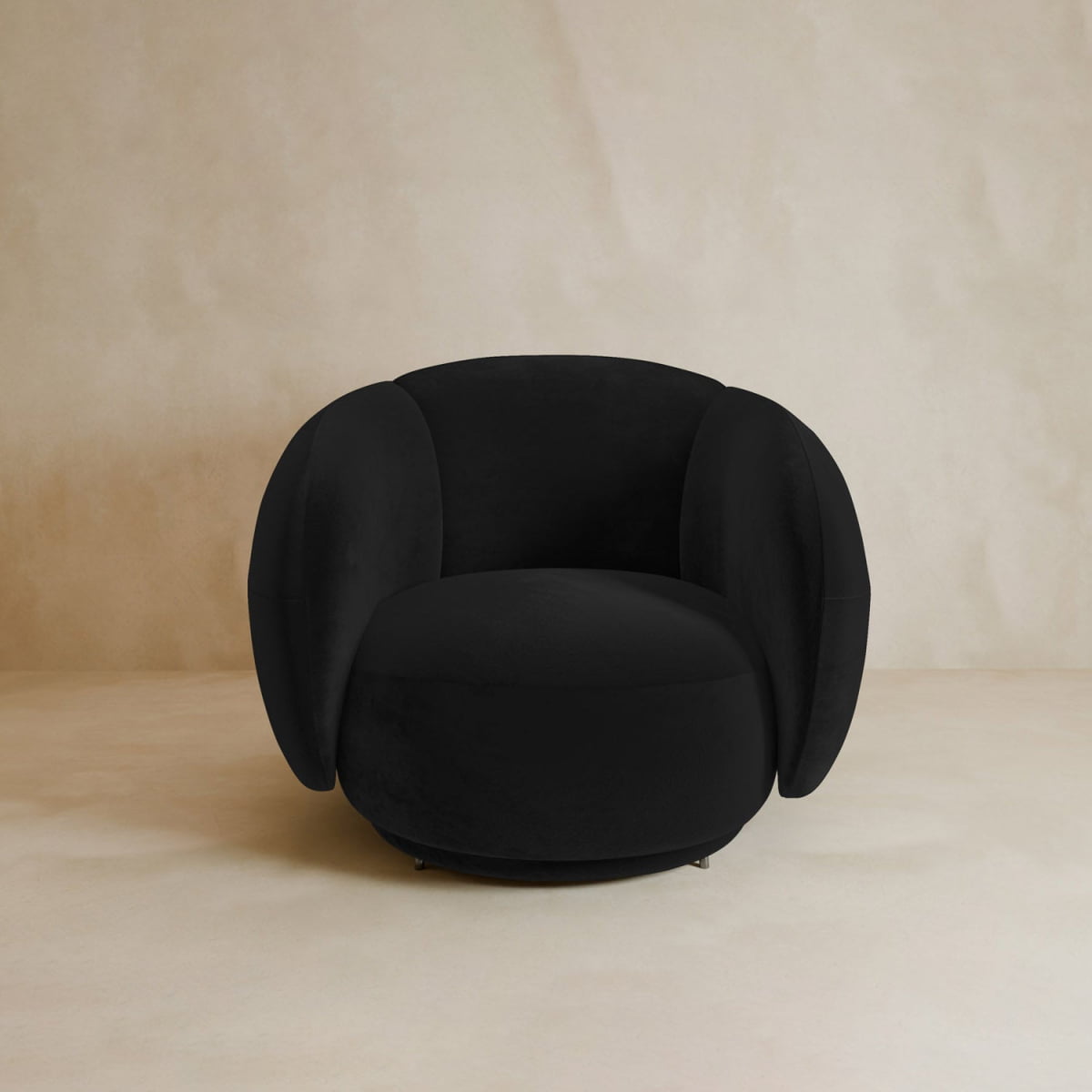 The Clara Armchair features a modern design in black with rounded, oversized armrests and a plush velvet backrest, set against a plain beige background.