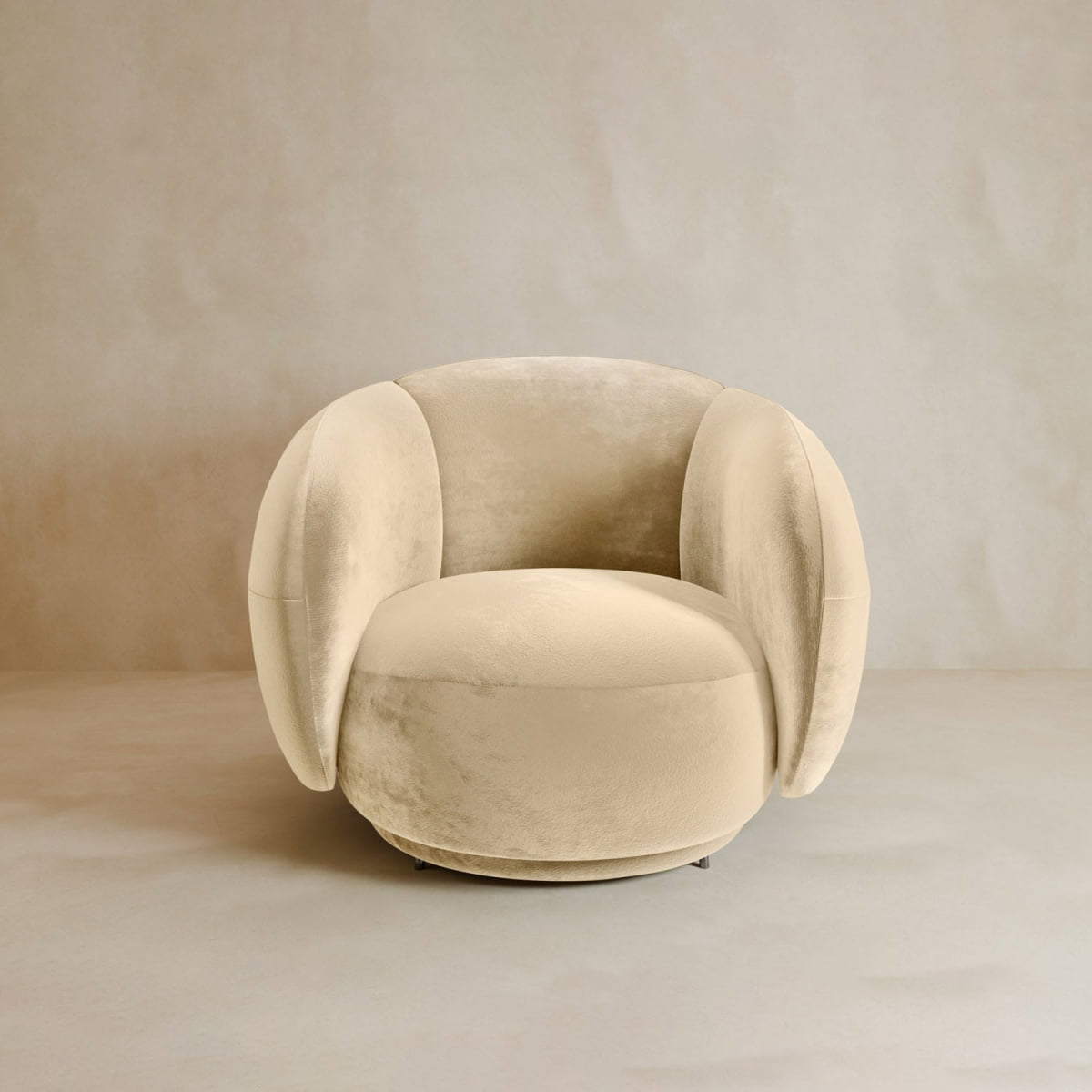 The Clara Armchair features plush, rounded beige velvet upholstery with soft curved armrests and backrest, perfectly complementing neutral-toned interiors for a refined contemporary look.