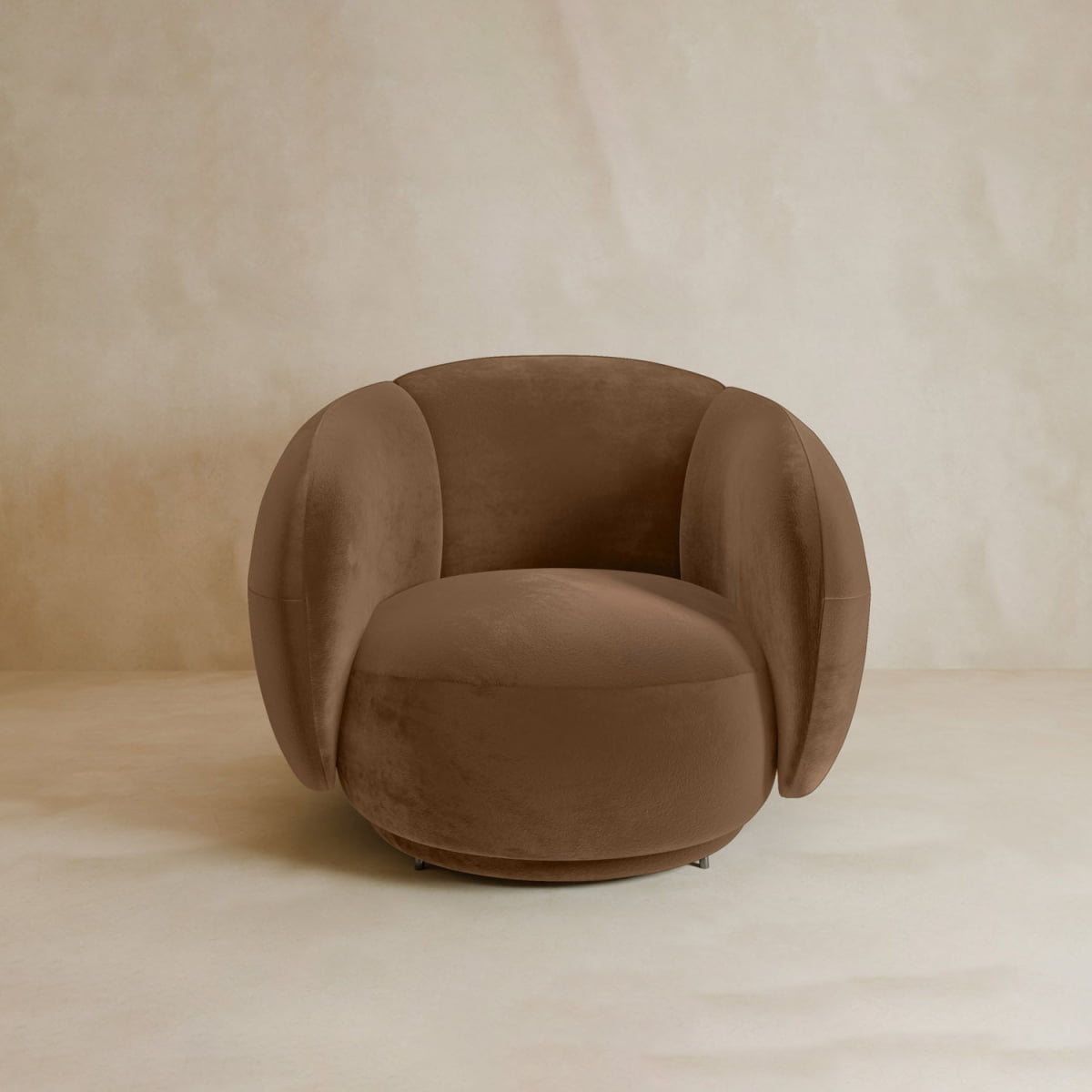 The Clara Armchair boasts contemporary style with plush velvet upholstery, rounded oversized arms, and a curved backrest in a neutral beige.
