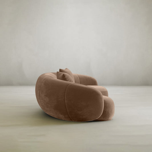 The Clara Sofa features modern, plush brown upholstery and rounded pillow-like shapes, making it an ideal centerpiece for contemporary homes. It stands out beautifully against a pale gray wall and a smooth, light-colored floor.