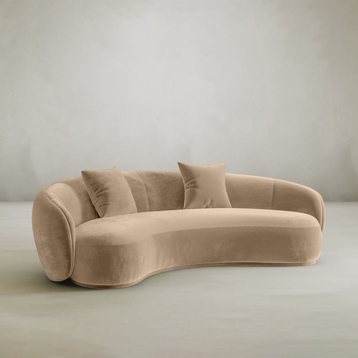 The Clara Sofa features a curved beige velvet design with three matching cushions and a rounded back, set against a light grey background—perfect modern comfort for any contemporary home.