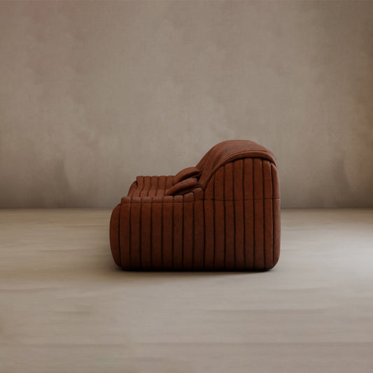 The Calypso Armchair, featuring modern brown corduroy upholstery and a curved, tufted stripe design, adds elegance to any room. Its low profile looks stunning on a light floor beside a plain beige wall.