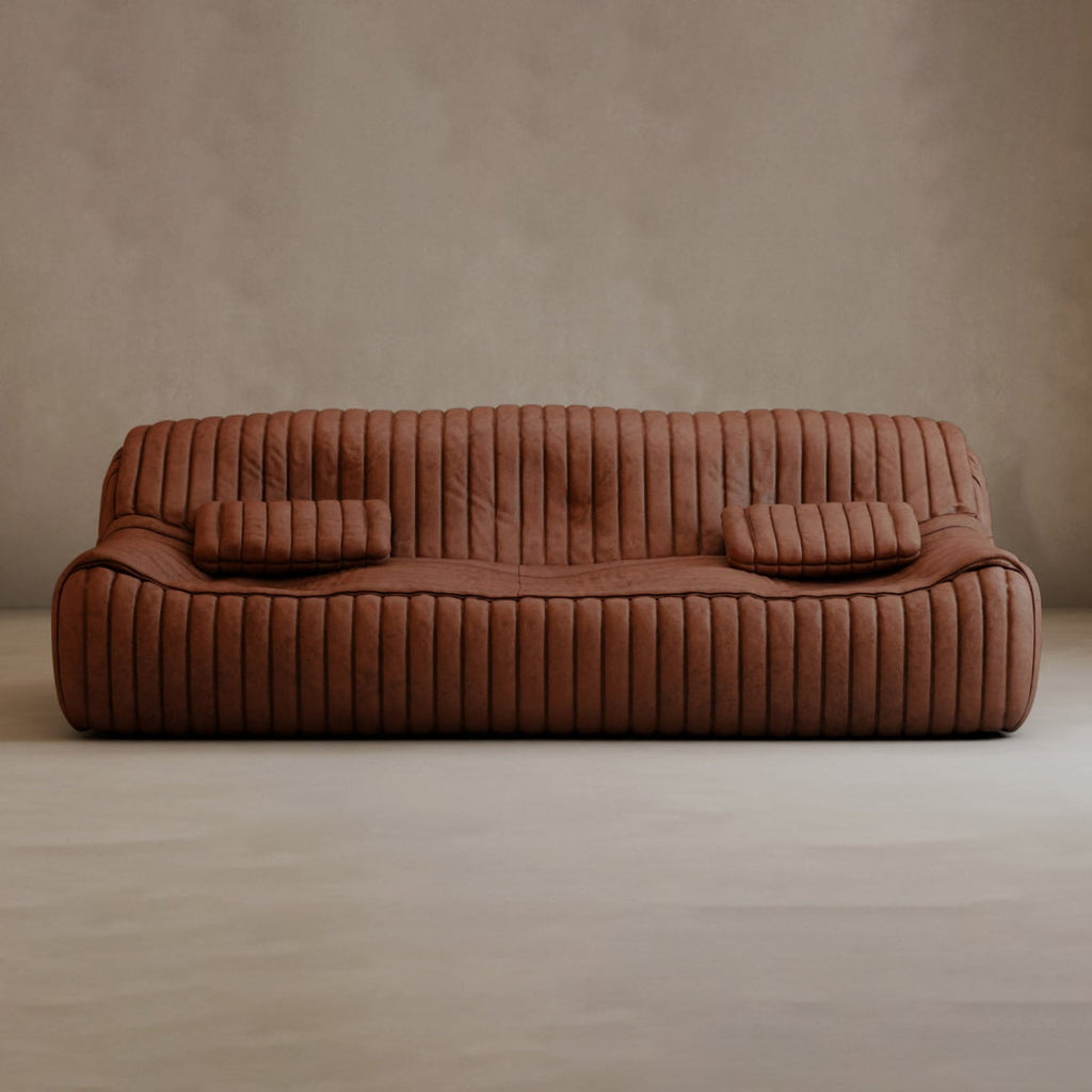 A modern, low-profile Calypso Armchair with vertical ribbed upholstery and two matching rectangular cushions, exuding modern elegance against a plain beige wall and light floor.