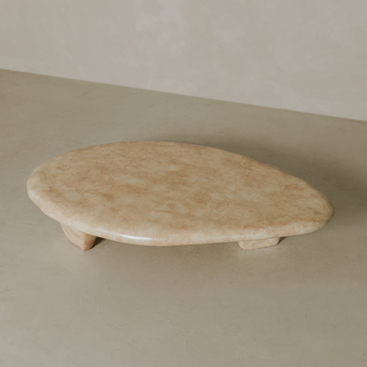 The Cleo Coffee Table features a smooth, oval beige stone top with short legs, showcased on a neutral surface and set against a light, textured background.