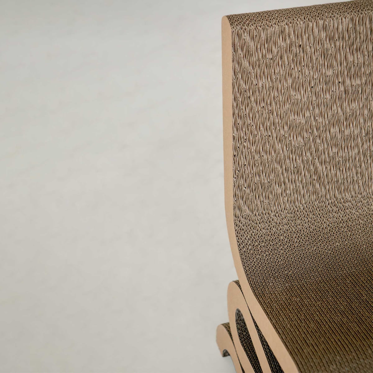 Close-up of the Curly Wurly Chair, a modern piece crafted from layered, corrugated cardboard. Its curved backrest and seat highlight the intricate texture of cardboard against a simple light background.
