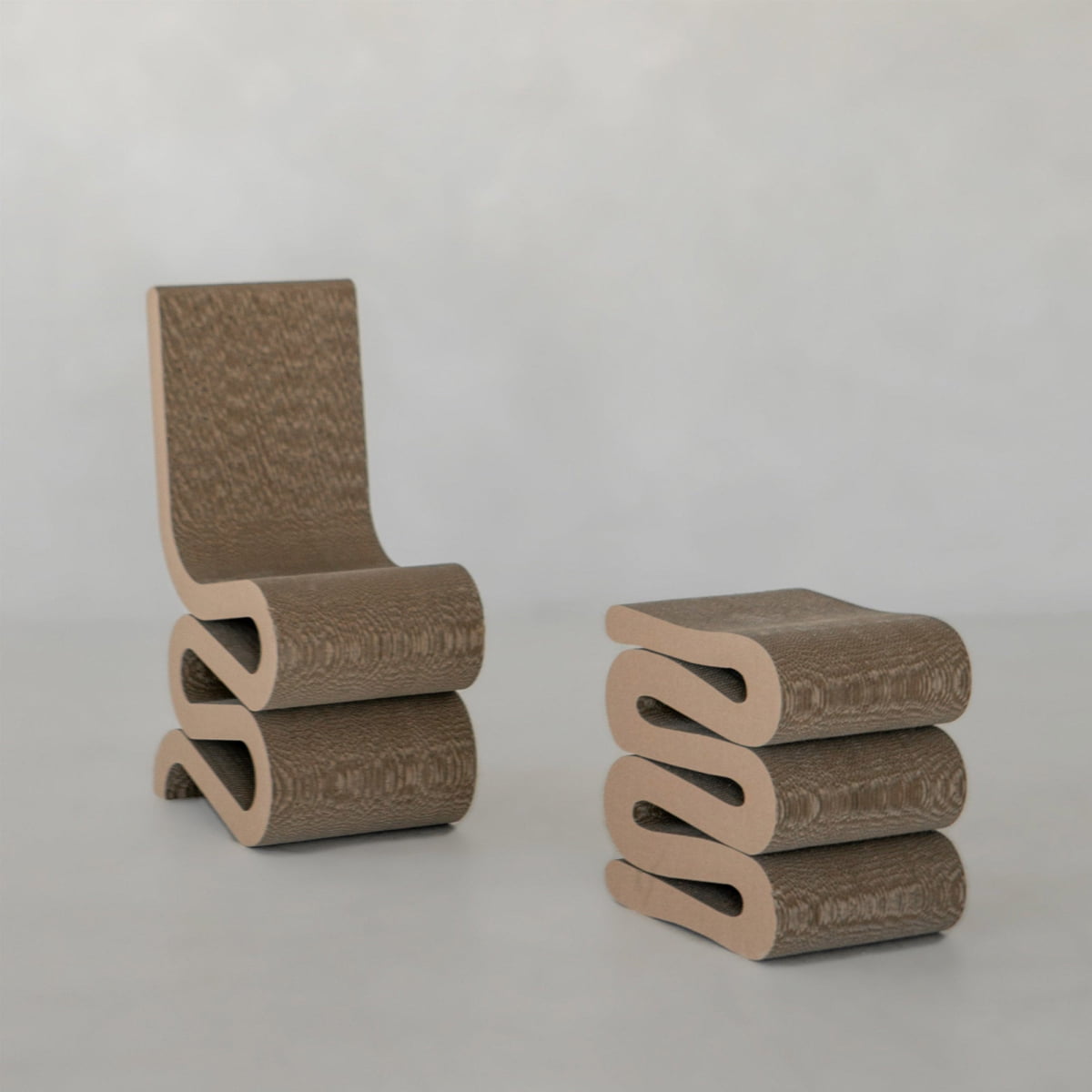 The Curly Wurly Chair and matching ottoman showcase sculptural, wavy, layered cardboard designs, set against a plain light background.