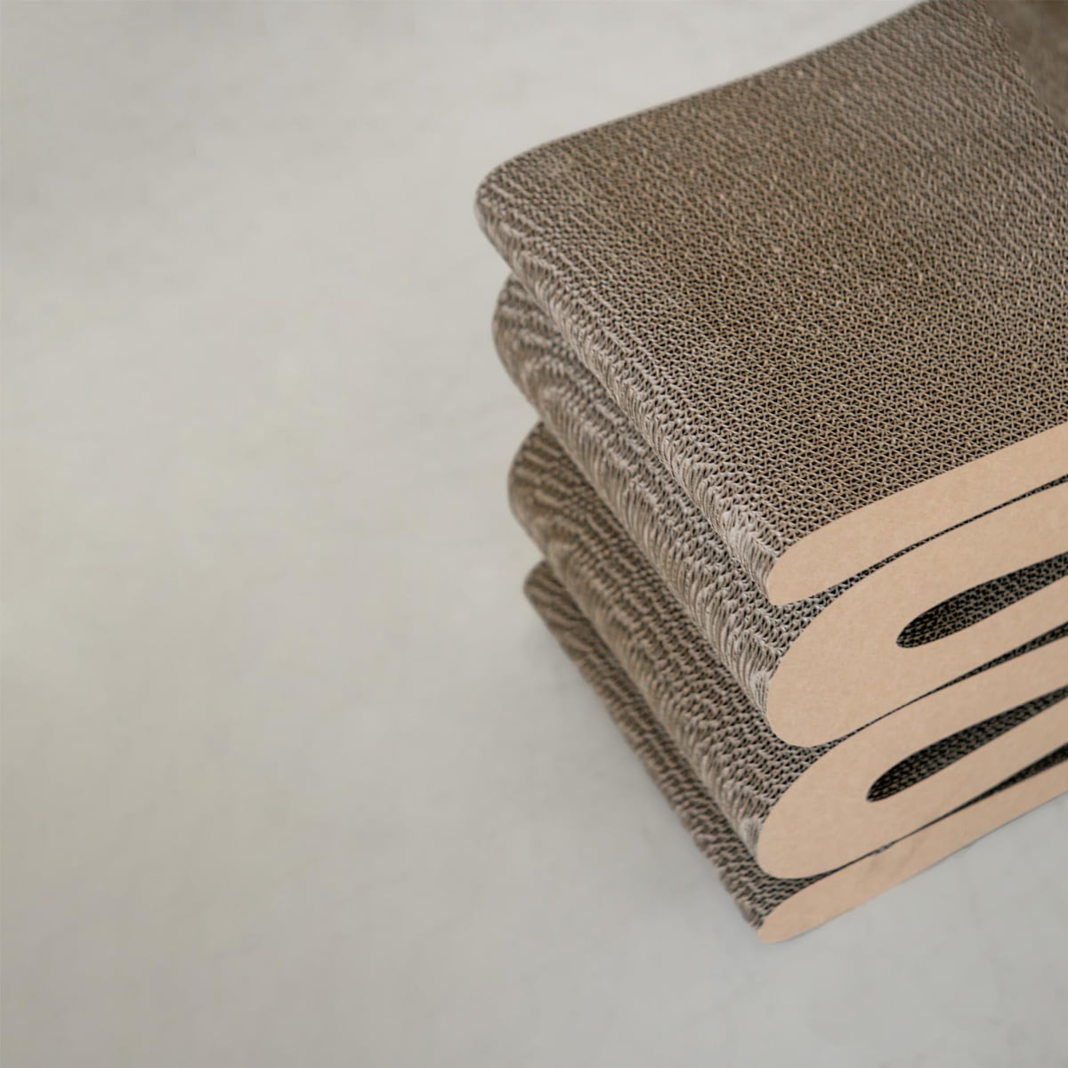 A close-up view of three stacked Curly Wurly Chairs for cats, featuring multiple cardboard layers with a corrugated texture and curved edges, placed on a light, neutral background.