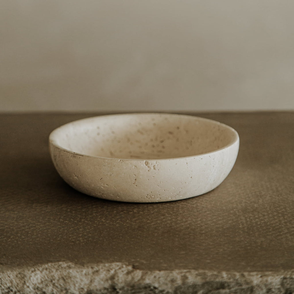 The Étoile Bowl in Medium, crafted from premium travertine with a textured surface, sits on a rough brown tabletop, showcasing French elegance against a neutral background.