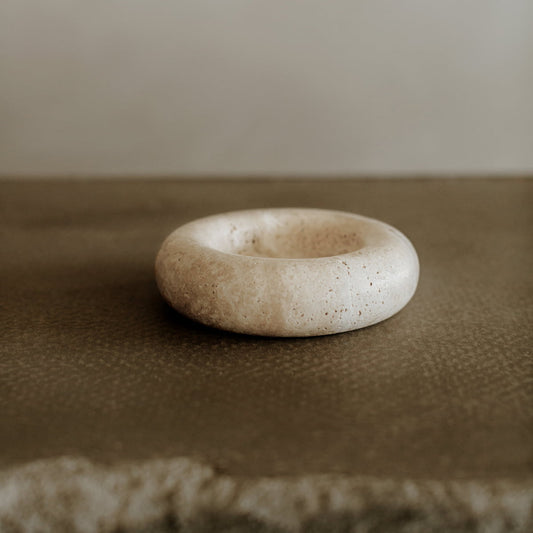 The Étoile Bubble Tray, with its smooth, round travertine design and shallow center, exudes French elegance as it rests on a textured brown surface against a plain, light background.
