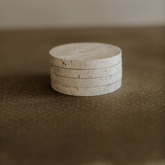 The Étoile Coaster Set of 4 features round, light-toned travertine coasters that add French elegance and sophistication to any space, effortlessly blending style on a brown textured surface with a neutral backdrop.