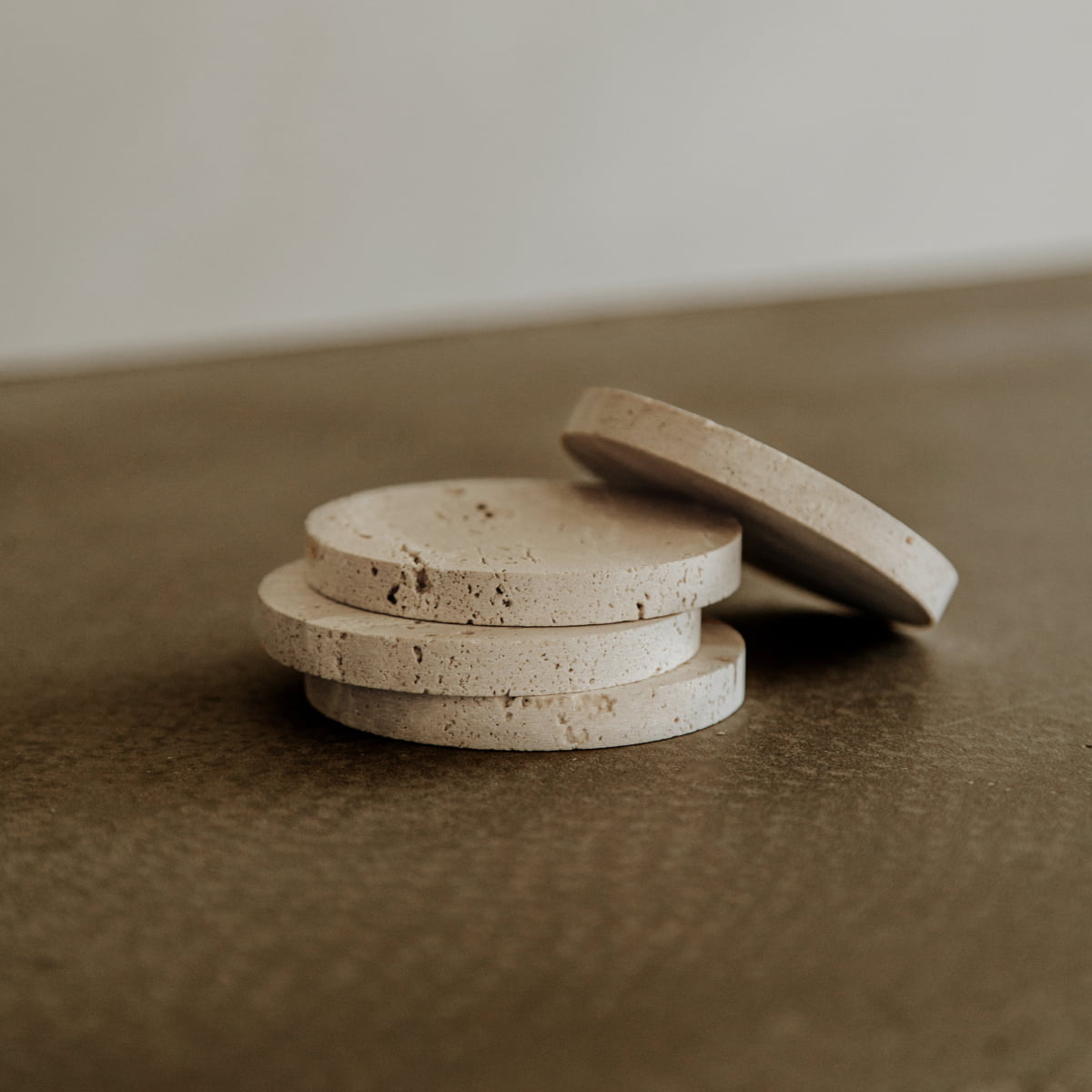 Four round, beige Étoile Coaster Set of 4 with textured surfaces are stacked on a brown tabletop. Arranged at slight angles, they bring French elegance and the allure of premium travertine to your space.