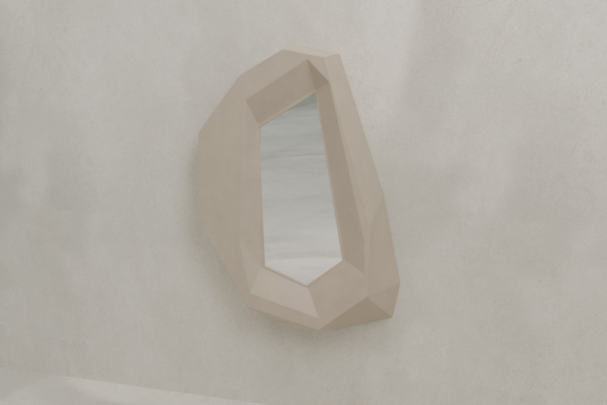 The Facet Mirror Large, featuring an irregular geometric frame with a faceted beige border, hangs on a plain light wall and reflects a subtle minimal scene, bringing modern sophistication to the space.
