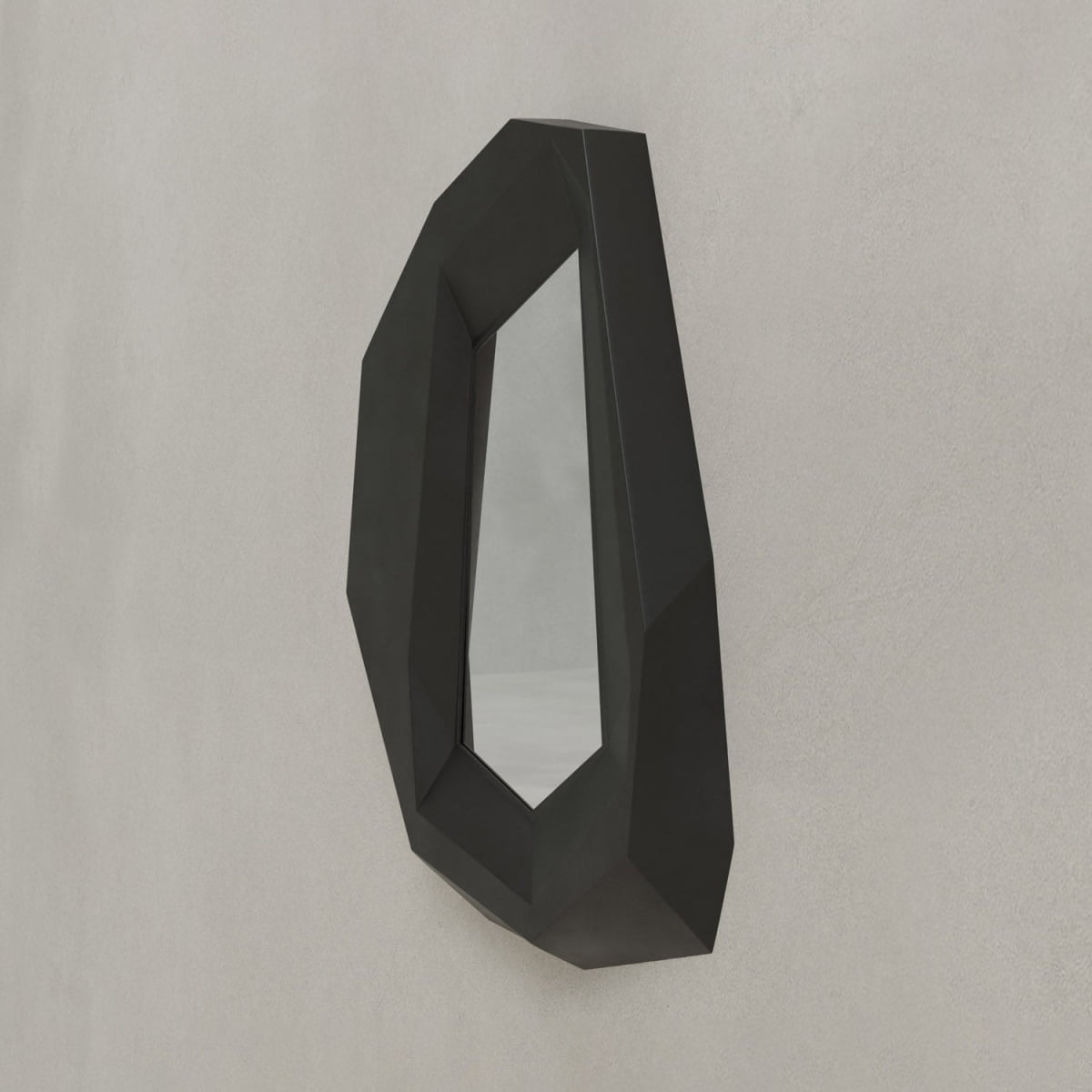 The Facet Mirror Small features a black frame and angular, faceted edges, adding modern sophistication to a light gray textured wall. Its sculptural silhouette offers a bold hint of brutalist design for striking contemporary style.
