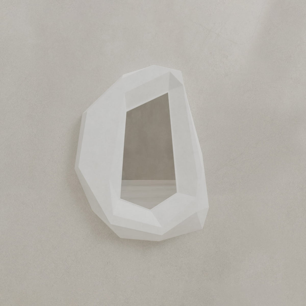 The Facet Mirror Small, featuring a geometric, irregular design and faceted white frame, adds modern sophistication with its crystal-inspired form and angular edges, subtly nodding to brutalist style when mounted on a light beige wall.