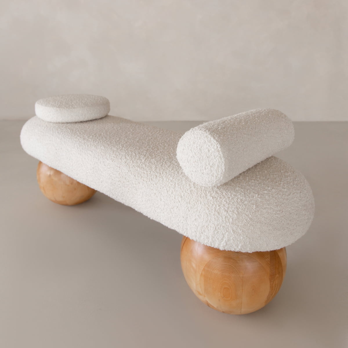 The Finchley Bench features textured white upholstery, cylindrical end cushions, and three large wooden sphere legs, bringing modern sophistication to any contemporary space with its sleek design.