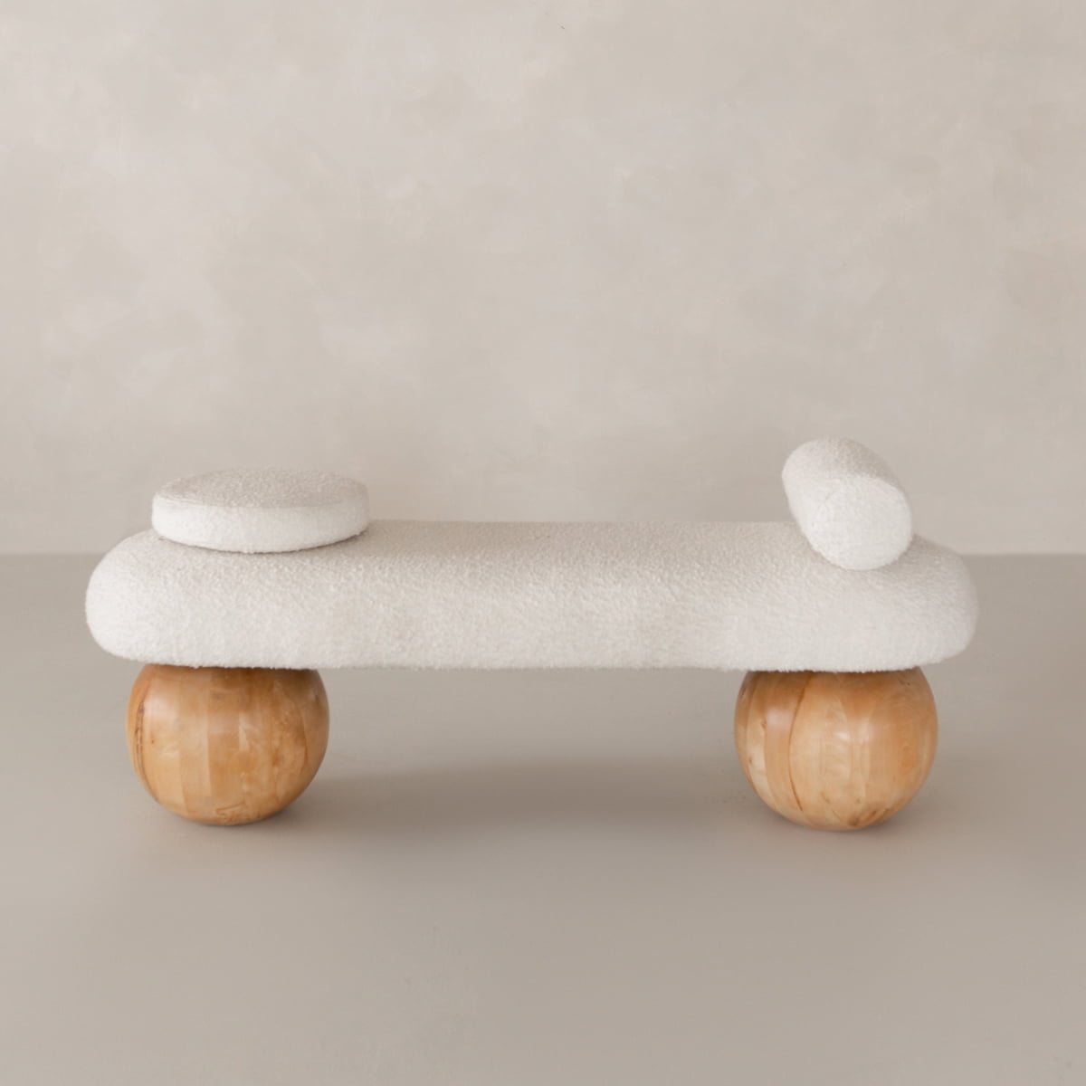 The Finchley Bench features white textured upholstery, two round cushions, and spherical wooden legs, making it a stylish addition to contemporary spaces with its modern sophistication.