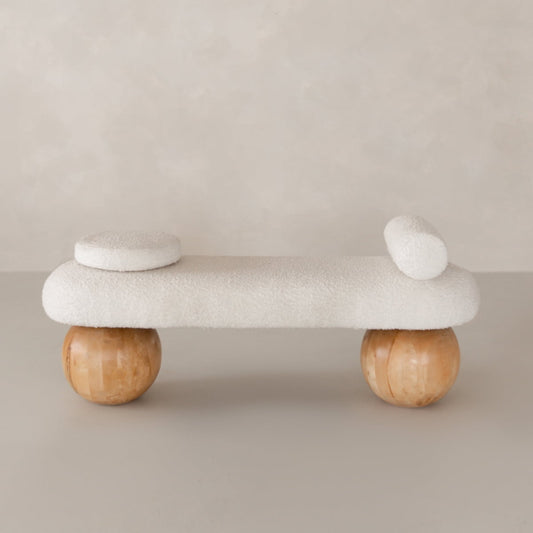 The Finchley Bench features white textured upholstery, two round cushions, and spherical wooden legs, making it a stylish addition to contemporary spaces with its modern sophistication.