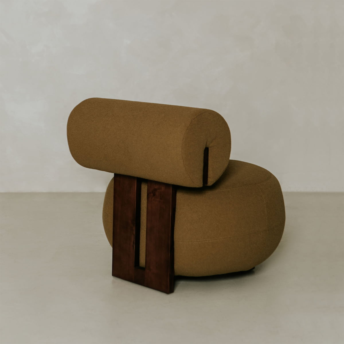 The Finchley Chair features a modern brown design with a cylindrical backrest, round cushioned seat, and two vertical solid legs in a dark wood finish, ideal for minimalistic rooms with light walls and floors.