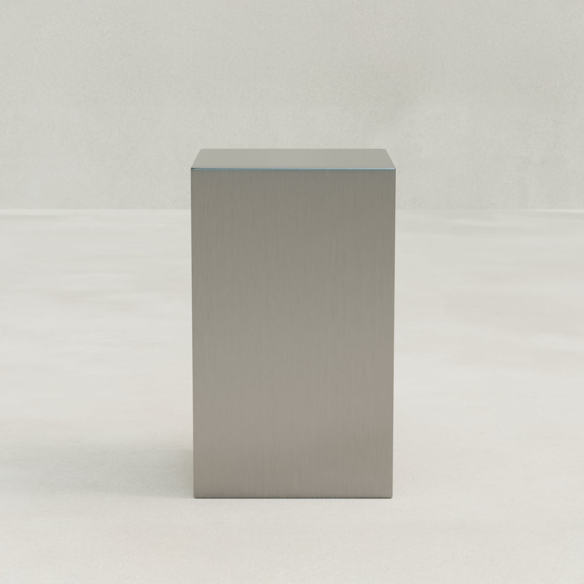 The Forge Steel Tall Plinth stands on a smooth, light-colored surface against a pale background, adding modern design and subtle industrial flair to the space.