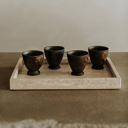 Four small, dark ceramic cups sit on the Grande Cascade Tea Tray, their elegant forms contrasting beautifully with the tray’s textured surface and neutral background.