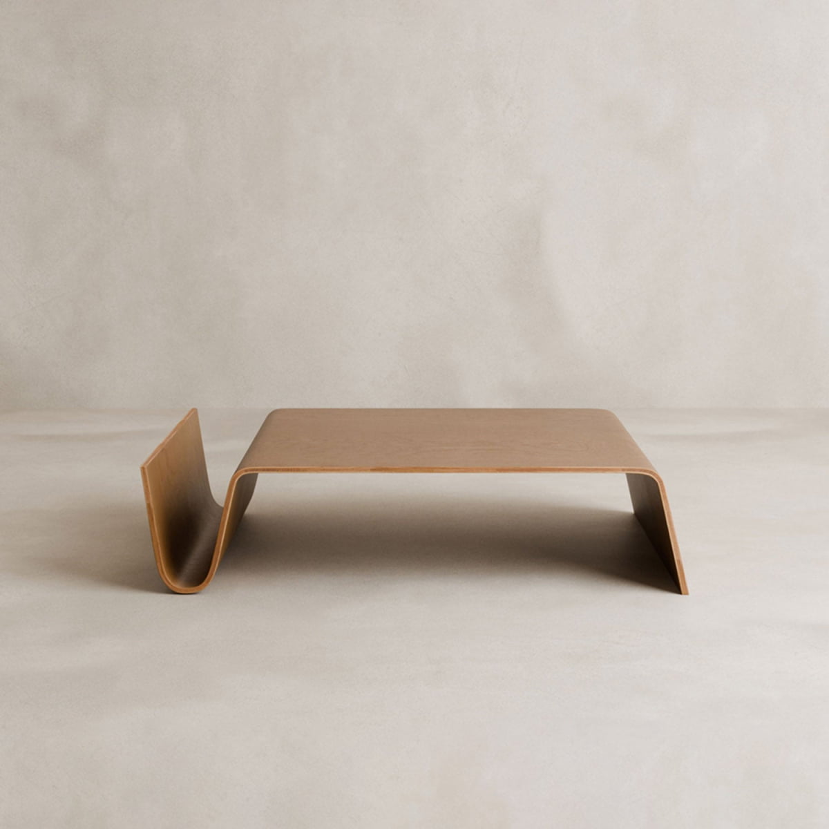The Gregory Coffee Table features a minimalist, modern design with a light wood finish and unique wavy form—one end curves upward while the other is vertical. It adds style to any space and doubles as an eye-catching magazine shelf.