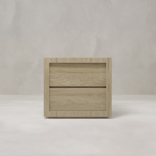 The Henley Nightstand, a minimalist oak piece with two drawers and a light wood finish, stands against a plain, light-colored background.
