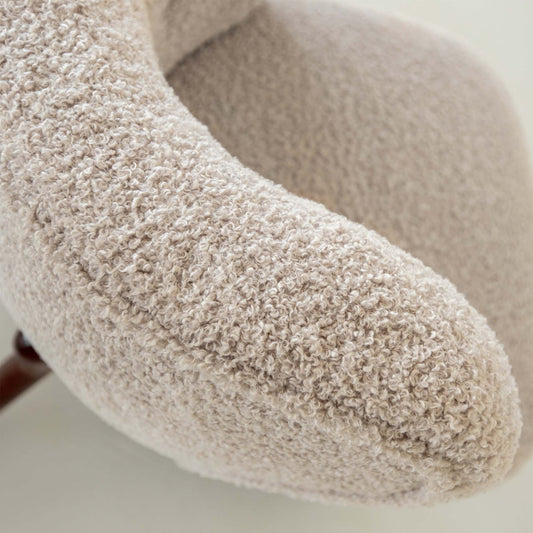 Close-up of the Highgate Chair, a curved armchair upholstered in textured beige boucle fabric, with soft rounded contours and a visible seam along the armrest—a contemporary statement piece for any space.