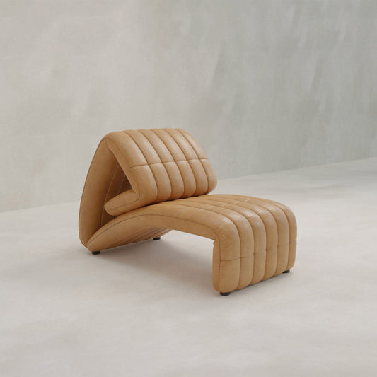 The Hillier Chair features premium vintage leather, a sculptural wavy design, and vertical stitching, shown on a light floor against a pale textured wall.