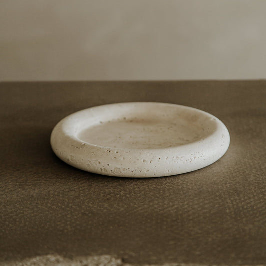 The Janvry Tray, a round shallow piece with a textured surface, rests on a brown, rough-textured tabletop, seamlessly blending style and functionality against a neutral background.