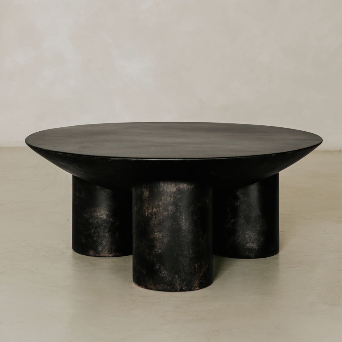 The Luna Coffee Table is a modern black round fiberglass piece featuring a thick top and four wide tubular legs, set against a plain, light background—ideal for contemporary interiors.