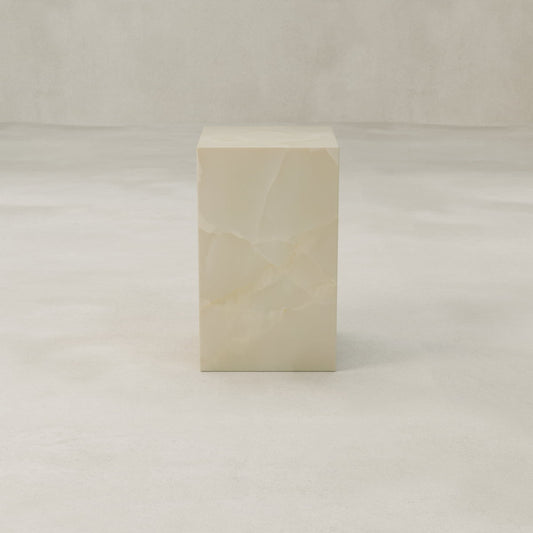 The Lunelle Onyx Tall Tower Plinth, featuring a smooth, polished milky surface, stands out as a sculptural centerpiece on a light textured floor against a neutral background.