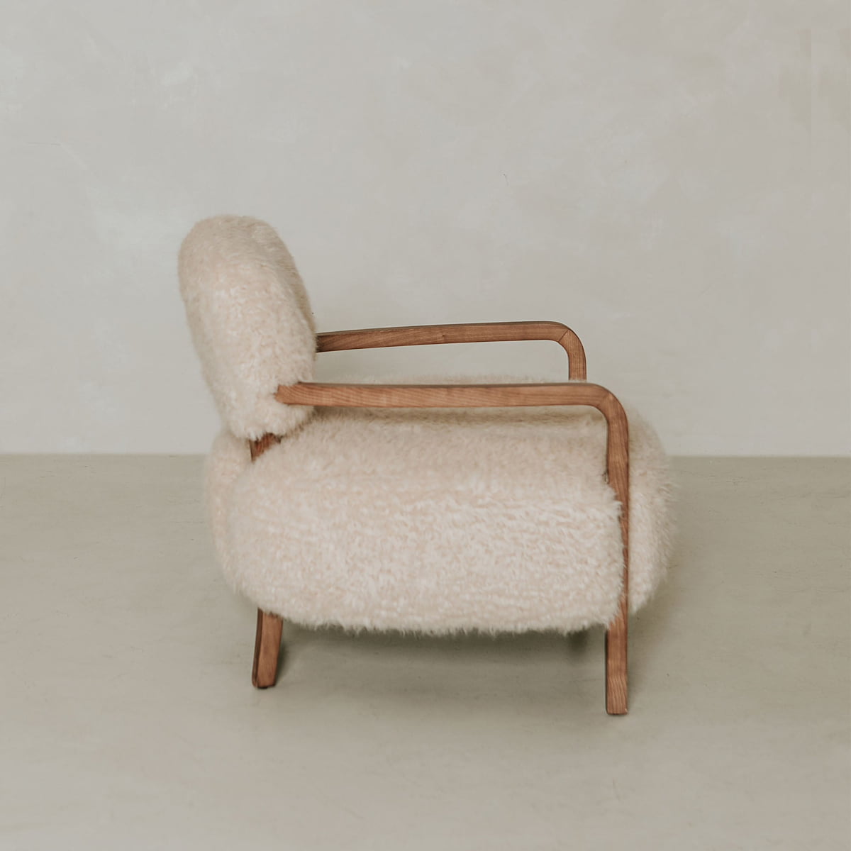 The Malmo Chair features modern design with fluffy shearling upholstery and curved wooden arms and legs, shown against a plain, light background.