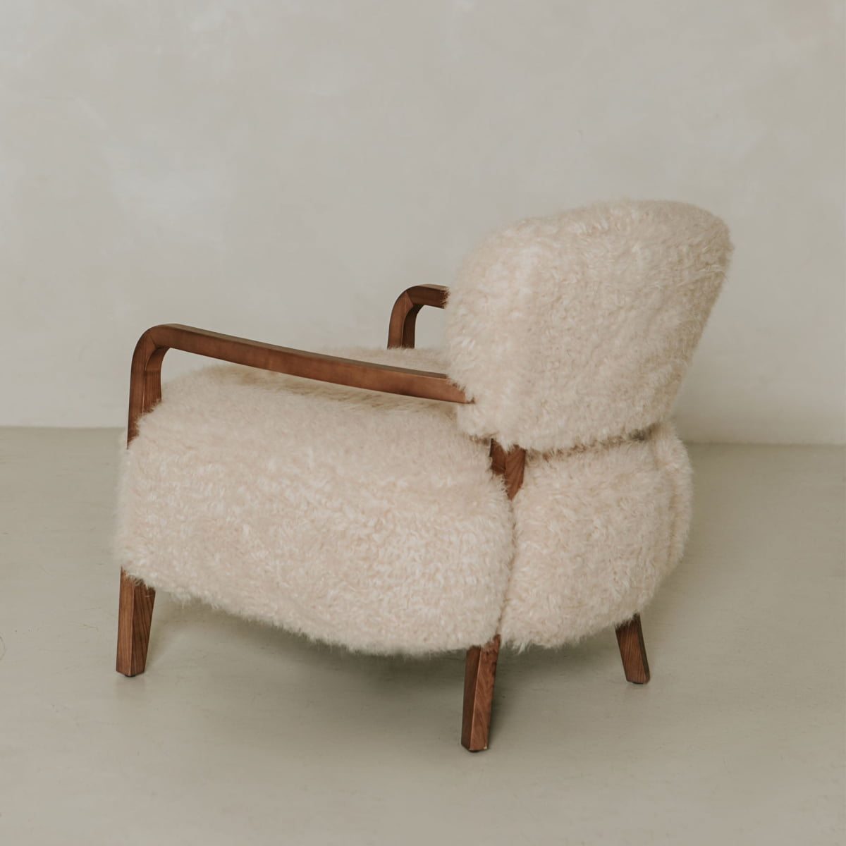 The Malmo Chair features wooden armrests and legs with plush cream shearling upholstery, offering minimalist sophistication against a plain, light background.