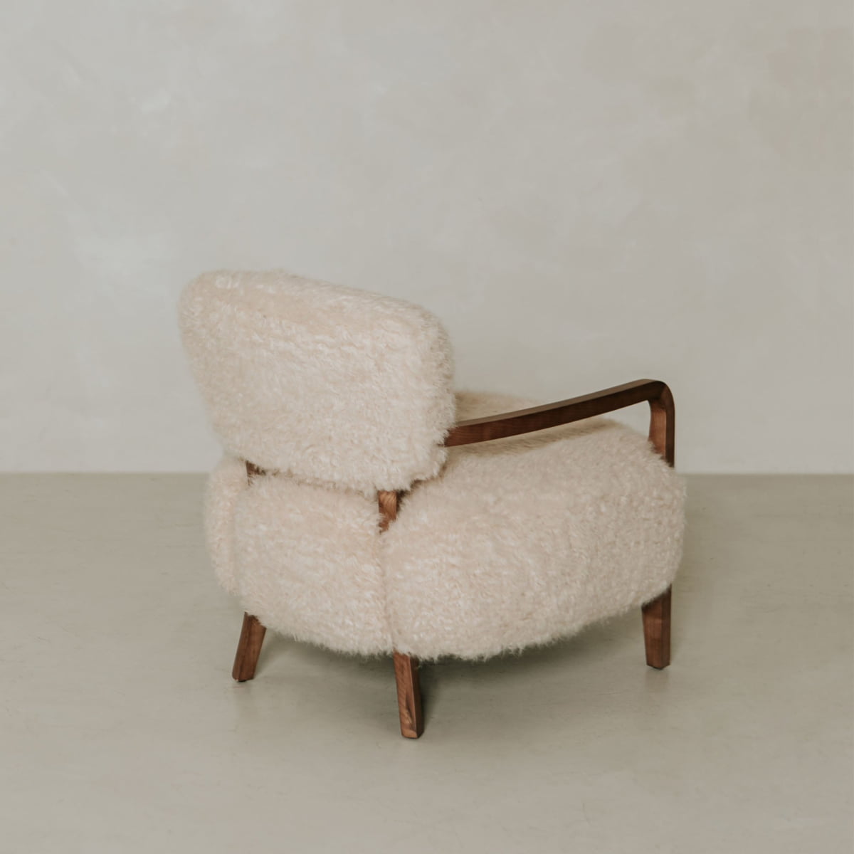 The Malmo Chair features light shearling upholstery and wooden armrests and legs, making it a modern piece that embodies minimalist sophistication in any room with light floors and walls.
