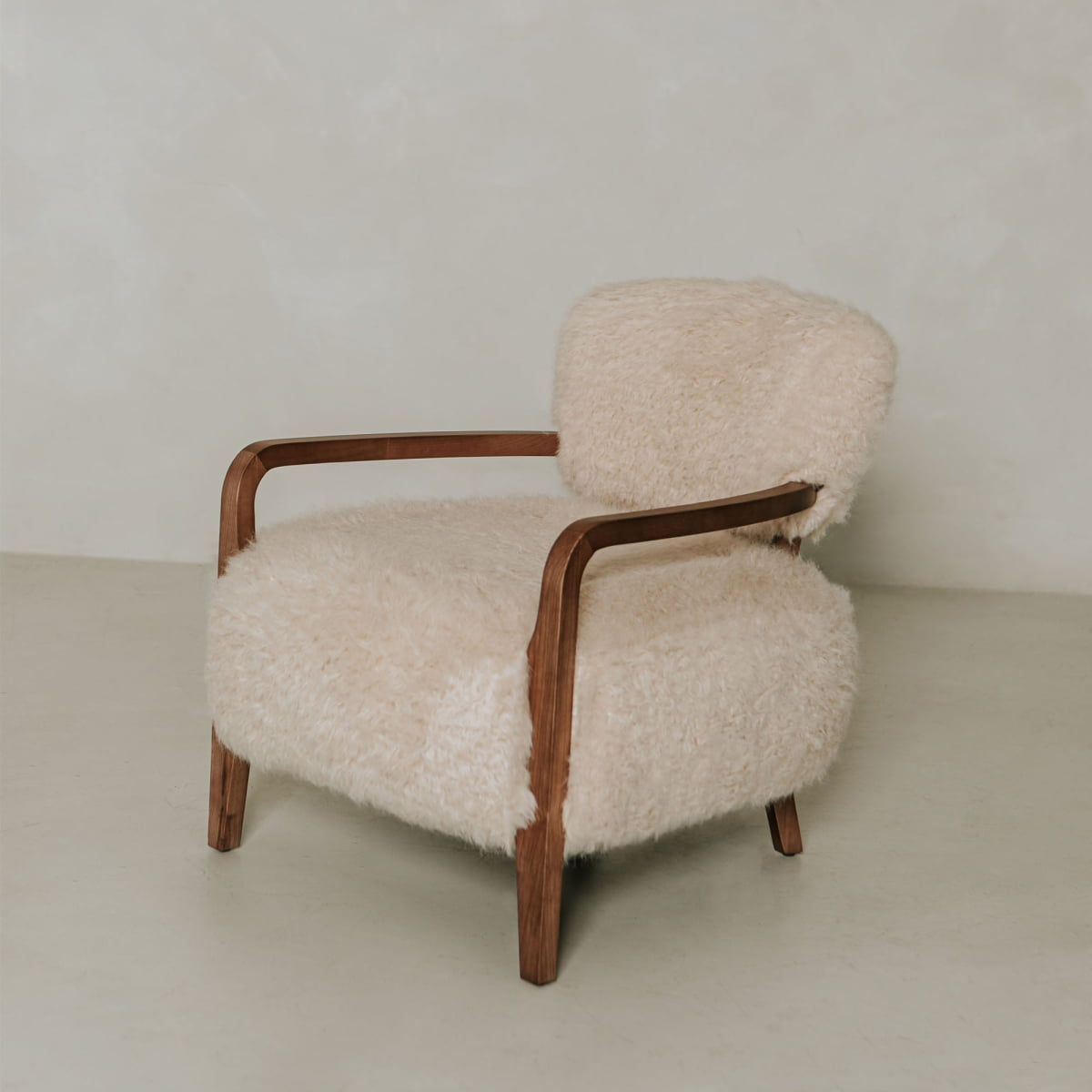 The Malmo Chair features wooden legs, curved armrests, and soft cream shearling upholstery, offering minimalist sophistication against a light background.