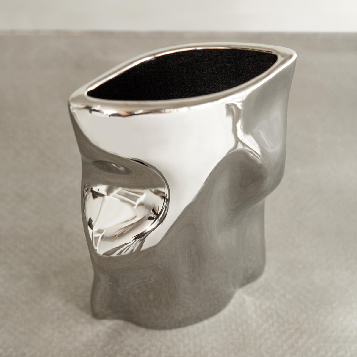 The Mira Vase features an abstract, organic shape with a polished chrome finish, offering modern sophistication and elegance against any neutral backdrop.