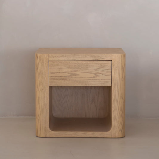 The Muswell End Table offers a minimalist look with light wood, a discreet drawer, and an open shelf—ideal for practical storage in any modern space.