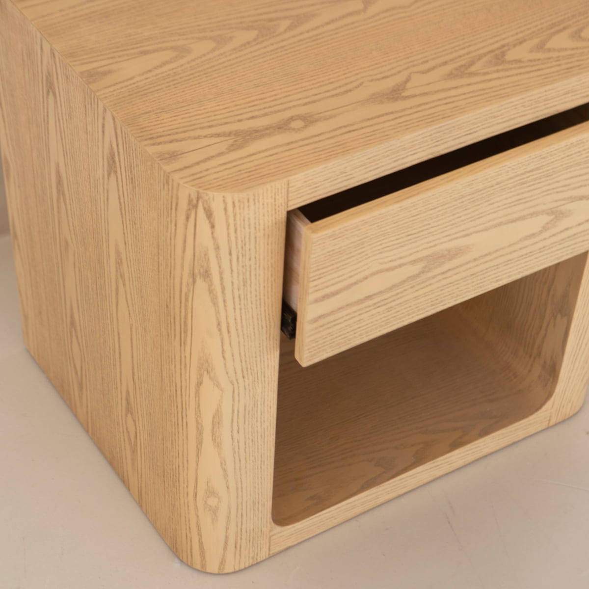 The Muswell End Table is a light wood nightstand with rounded edges, featuring a concealed drawer and an open lower shelf for convenient storage.