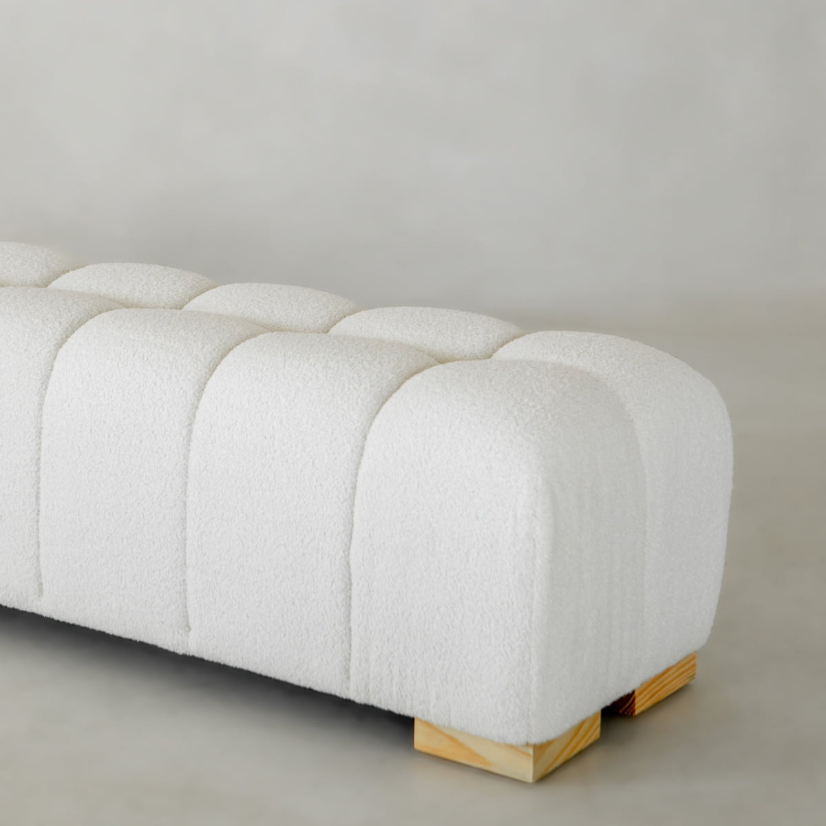 A close-up of the Olivia Bench shows its modern white tufted design, soft boucle fabric, and light wooden block legs set against a neutral background.