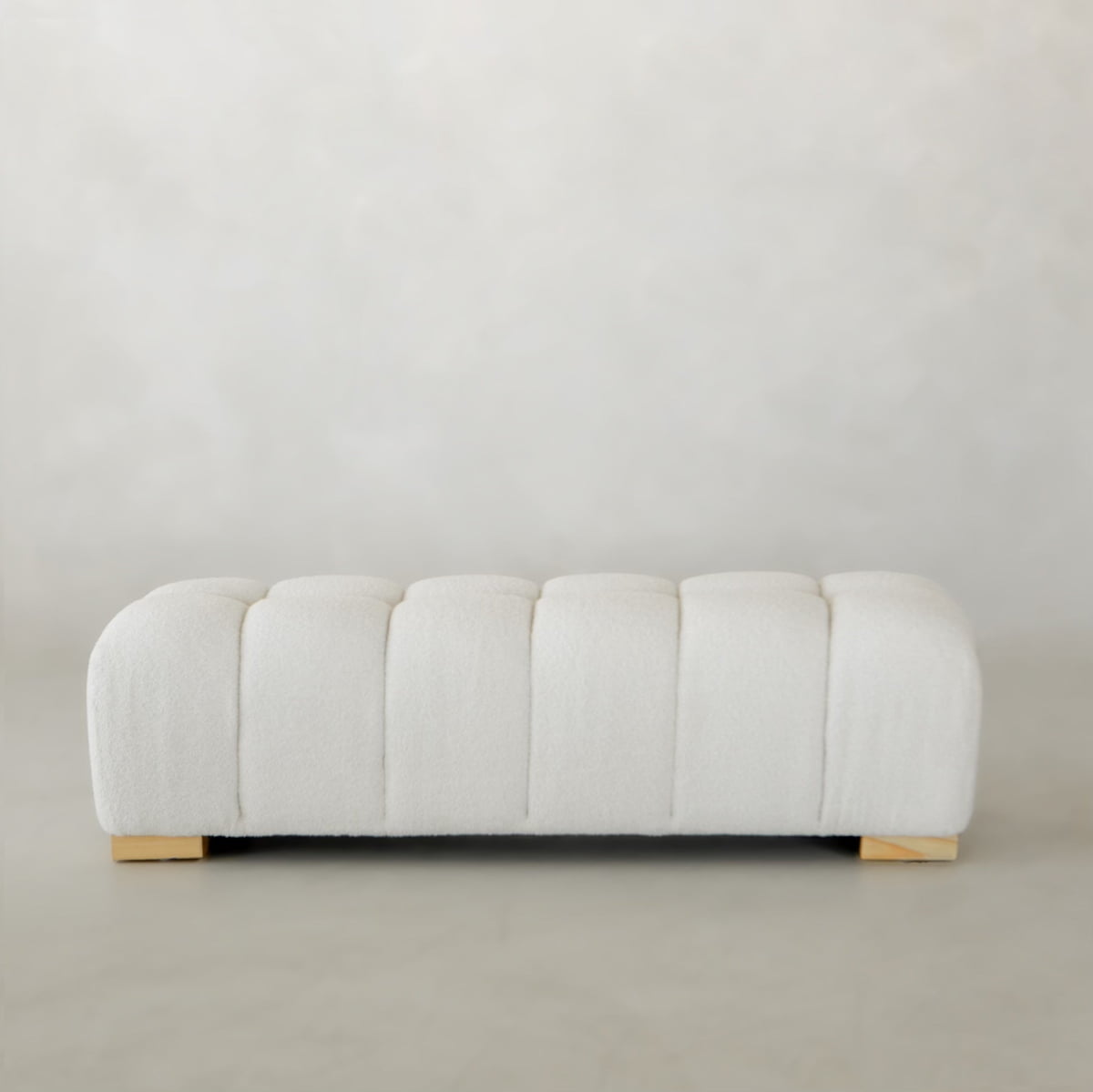 The Olivia Bench is a modern rectangular ottoman with tufted white upholstery and short wooden legs, styled for chic bench appeal. It sits on a light floor against a plain, light background.
