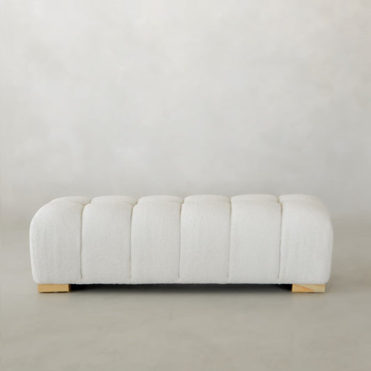 The Olivia Bench is a modern rectangular ottoman with tufted white upholstery and short wooden legs, styled for chic bench appeal. It sits on a light floor against a plain, light background.